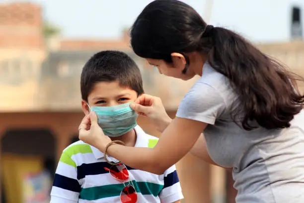 Young women puts on a child a medical protective mask before leaving the house.