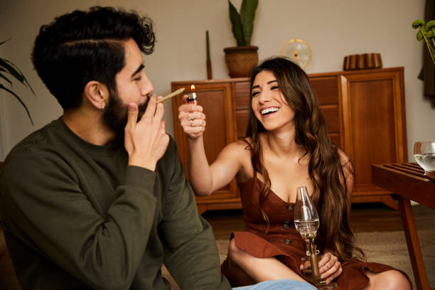 Laughing young woman lighting her boyfriend's joint Laughing young woman lighting a joint for her boyfriend while getting high together in their living room bong photos stock pictures, royalty-free photos & images