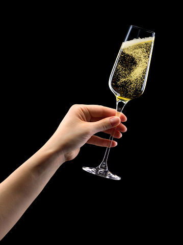 Woman hand holding glass of sparkling champagne isolated on black background.