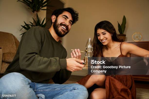 Young Couple Sitting At Home Smoking A Bong And Laughing Stock Photo - Download Image Now