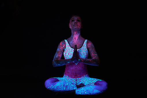 Woman does yoga, hand movement, body warm-up. Art girl cosmos in ultraviolet light. Entire body is covered with colored droplets. Astral yoga. Noise, out of focus