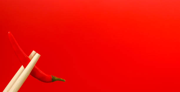 hölzerne essstäbchen halten eine hülse mit rotem paprika auf rotem hintergrund. das konzept des nervenkitzels. freier platz - the thrills stock-fotos und bilder