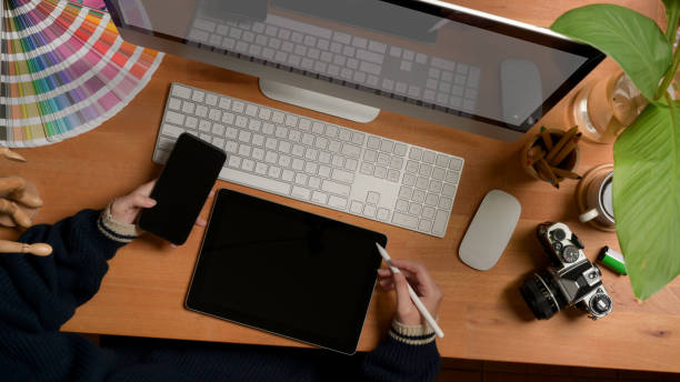 istock Female designer working with digital devices on wooden worktable with painting tools and supplies 1254520774