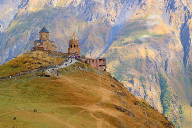 fantástica vista de la iglesia de la trinidad de gergeti o tsminda sameba en la cima de la colina con el monte kazbek en el telón de fondo, stepantsminda, georgia - georgia fotografías e imágenes de stock