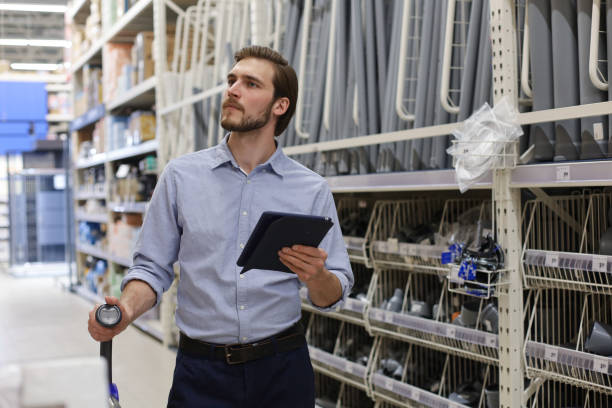 istock Young man shopping or working in a hardware warehouse standing checking supplies on his tablet. 1254528534