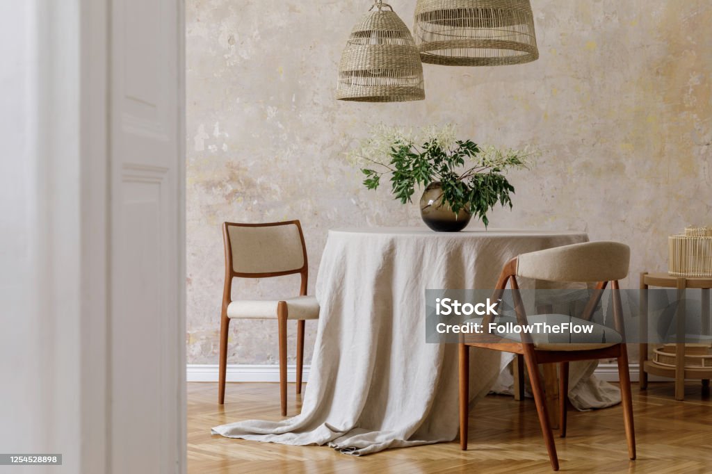 Stylish and elegant dining room interior with diner table, design chairs, rattan pendant lamps, dried flowers in vases, furniture, decoration and elegant personal accessories in cozy home decor. Apartment Stock Photo