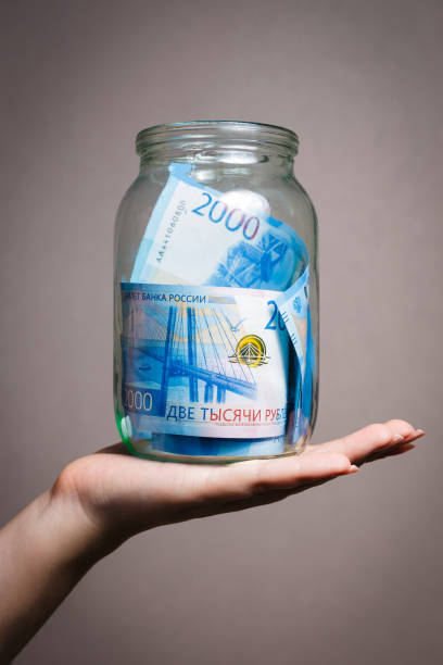 istock Glass jar with money on a human hand. Two thousandths Russian banknotes. 1254528986