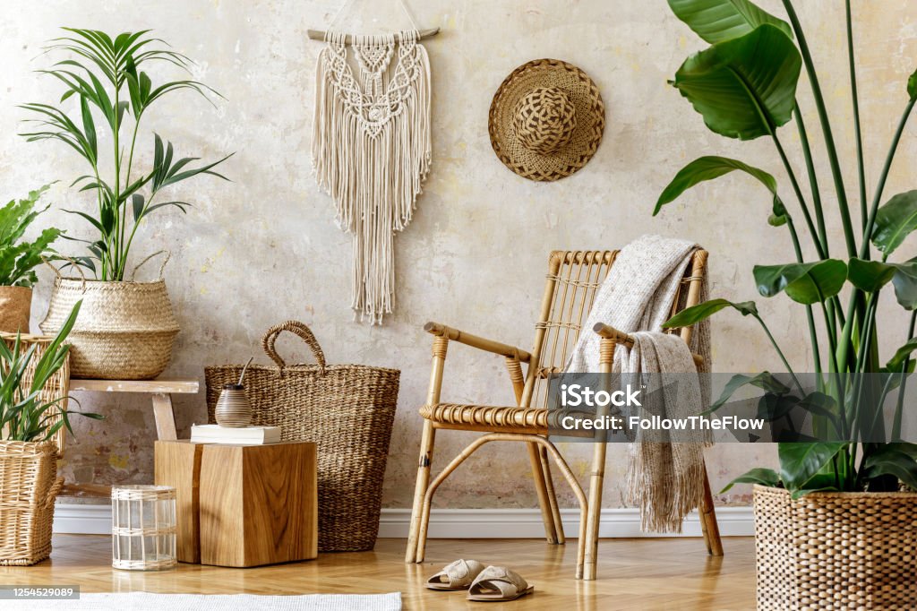 Stylish and floral composition of living room interior with rattan armchair, a lot of tropical plants in design pots, decoration, macrame and elegant personal accessories in cozy home decor. Stylish and floral composition of living room interior with rattan armchair, a lot of tropical plants in design pots, decoration and elegant personal accessories in cozy home decor. Wabi sabi concept. Home Decor Stock Photo