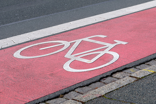 White bicycle symbol on a pink marking of a cycle path along a street in Nuremberg in Franconia / Bavaria, Germany. Seen in December.