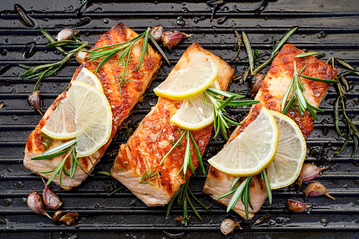 Grilled salmon fillets with fresh herbs and lemon slices on a grill,  top view