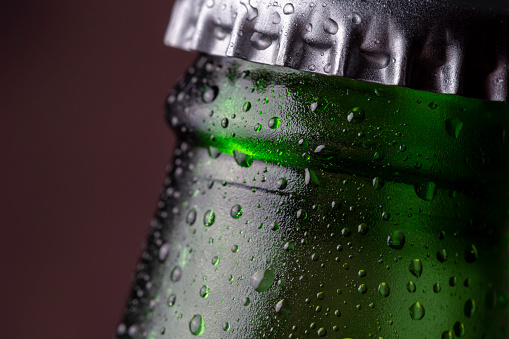 Detail of cold, wet beer bottle with a cap, dew and condensate water droplets on the surface of the glass