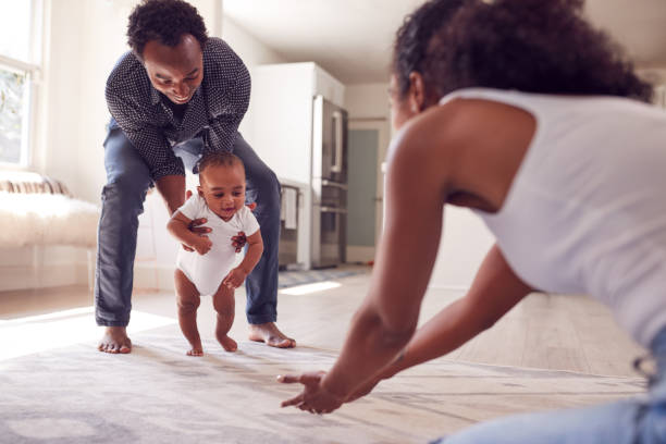 parents encourageant la petite fille souriante à faire les premiers pas et à marcher à la maison - grands évènements de la vie photos et images de collection