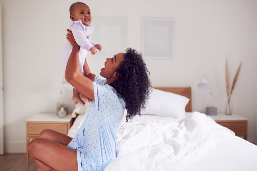 Loving African American Mother Wearing Pyjamas Playing Game With Baby Daughter In Bedroom At Home