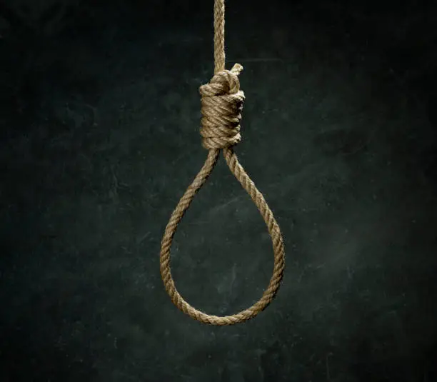 Photo of Rope noose for hangman made of natural fiber rope over black concrete wall. Hemp rope knot for gallows and Hang man on a grainy gray wall. The rope noose against the glum background, homicide or commit suicide concept