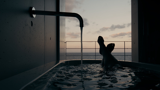 Beautiful photography of a woman silhouette lying in a luxurious bathtub with a view on the sea. Perfectly usable for all spa, wellness, self-love and relaxation subjects.