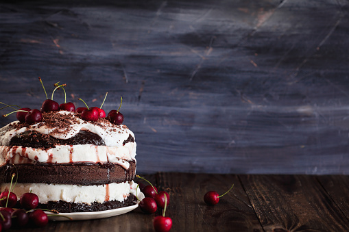 Delicious Black Forest Cherry Cake, Schwarzwald pie dessert, over a dark rustic wood table. Selective focus with blurred background and free space for text.