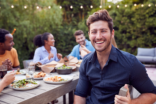 Portrait Of Man With Friends At Home Sitting At Table Enjoying Food At Summer Garden Party