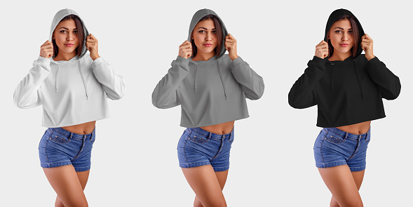Mockup of white, gray, black crop top on a beautiful girl in blue shorts, wearing a hood, front view, set of an empty pullover for presentation of design and pattern. Template hoodie on the background