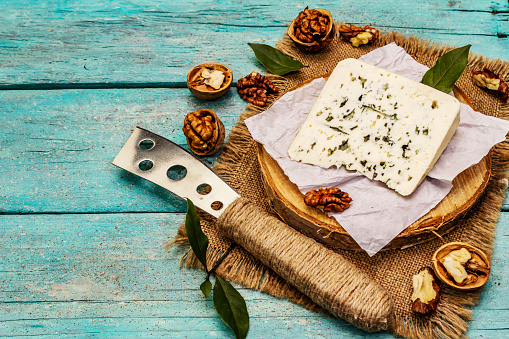 Cheese with blue mold. Ingredient for a cheese plate. Nuts, fragrant bay leaves, knife. Trendy turquoise wooden boards background, copy space