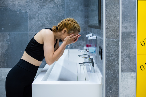 A female athlete washing her face and catching her breath in the locker room after an intense training session.