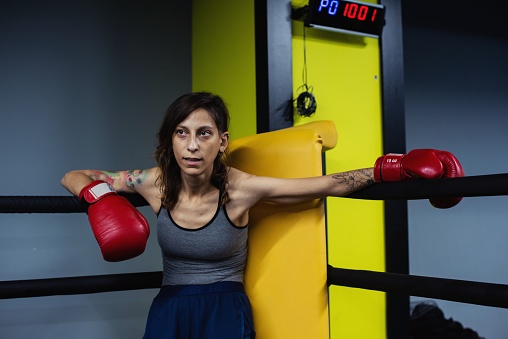 A female muay thai practitioner taking a break in one corner of the ring  after a sparring session.