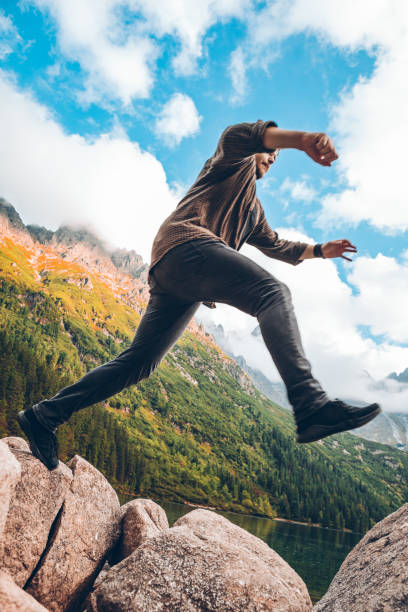 istock man jumping from rock at lake beach in mountains 1254562397