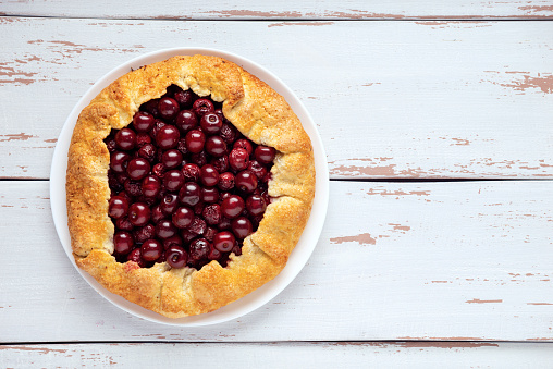 Galette with ripe red cherry filling on white background. Homemade sweet open pie on Provence style wooden background. Top view. Space for text.