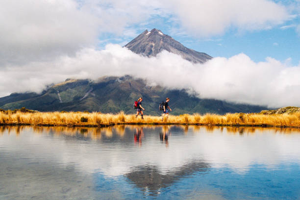 Hikers Reflection of Mount Taranaki Egmont in natural lake middle stock photo