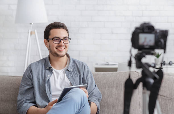 istock Famous blogger. Smiling young man with tablet in hands records video on camera 1254564496