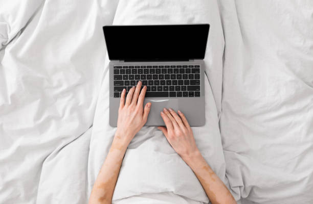 istock Woman working in bed and typing on laptop with blank screen 1254564525