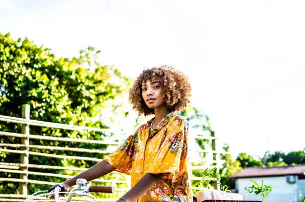 a young black woman in nature with a bicycle and a yellow shirt. looking at camera