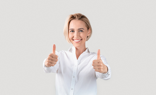 Cheerful business lady showing thumbs up gesture on light background, panorama