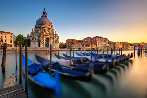 Long exposure photo of blue gondolas with the Basilica of Santa Maria Della Salute in the background on the Grand Canal in Venice.