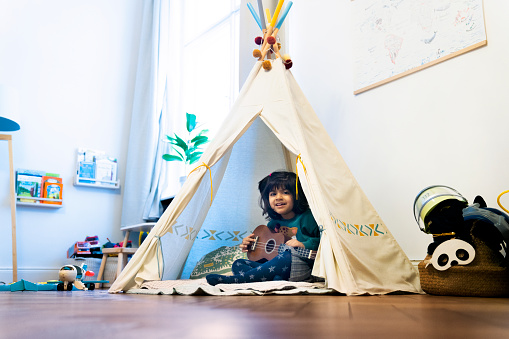 Cute girl sitting with ukelele in teepee tent