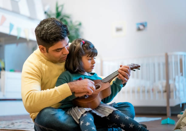 istock Man teaching daughter to play ukelele in bedroom 1254567160