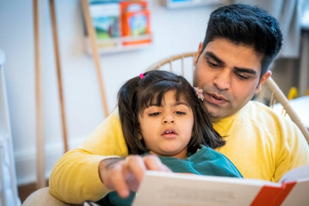 istock Father assisting daughter in reading book at home 1254567286