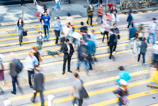 High angle view of male corporate professional in early 40s standing in middle of crosswalk on busy street checking smart phone in Hong Kong Central District.