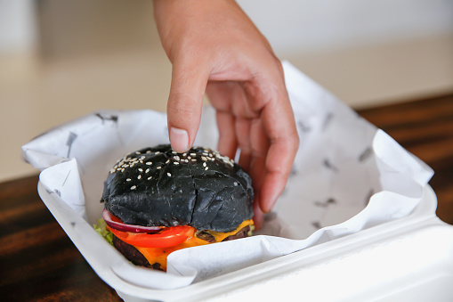 Close up shot of female hands taking a black activated charcoal hamburger from a styrofoam takeout box
