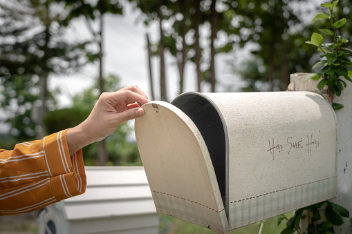 Hand putting a letter or a brown envelope in the mailbox in front of a house with copy space on the right side and on the envelope.