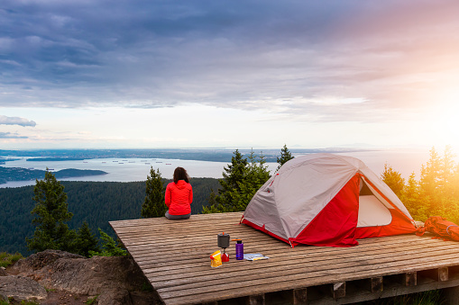 Adventure Girl and Camping Tent on top of a Mountain with Canadian Nature Landscape in the Background during colorful sunset. Taken on Bowen Island, near Vancouver, British Columbia, Canada.