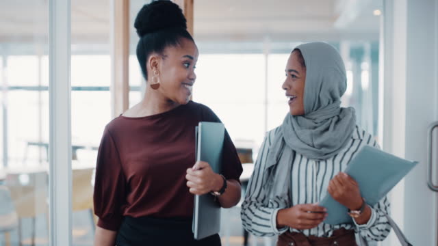 4k video footage of two young businesswomen having a discussion while walking through a modern office
