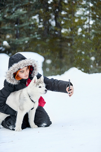 Shot of a teenage boy in warm jacket taking selfie with his pet husky dog outdoors on a winter day