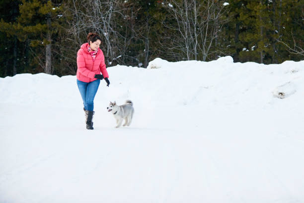 Shot of a woman playing with her pet husky dog on snowy landscape