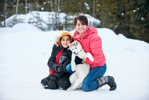Shot of a mother and son with their pet husky dog in snow outdoors