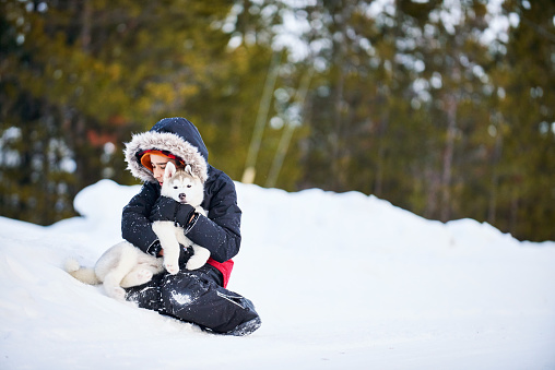 Shot of a little boy in warm jacket playing with his pet husky dog in snow outdoors