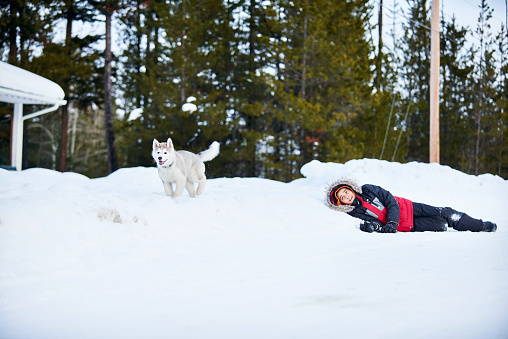 Shot of a boy playing with his pet husky dog in snow outdoors