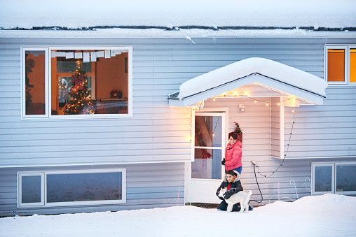 Rear view shot of a mother and son with their pet husky dog outside their house in a winter day