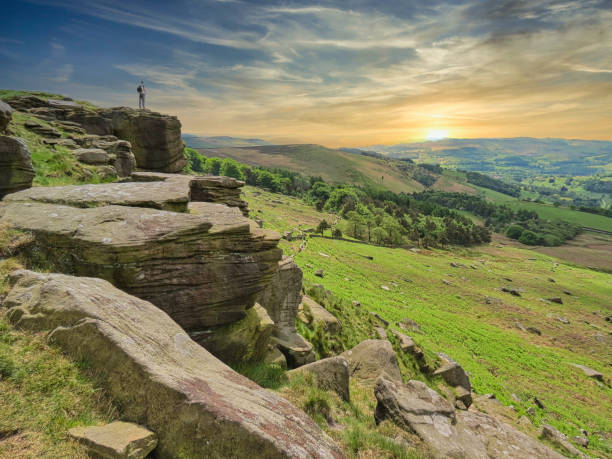 A man enjoys a sunset from the ridge at Stanage Edge in the English Peak District Stanage Edge is located to the north of Hathersage, Derbyshire in the English Peak District, and is a popular place for walkers and for rock climbing with stunning views of the Dark Peak moorlands and the Hope Valley. peak district national park photos stock pictures, royalty-free photos & images