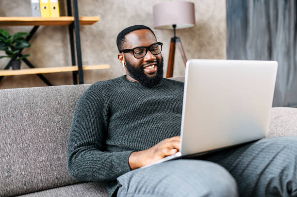 istock African-American guy sits on sofa with laptop 1254577038