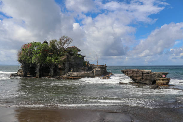 ondas se despedaçam em um penhasco no topo do qual é o templo hindu de tanah lot. templo construído sobre uma rocha no mar ao largo da costa da ilha de bali, indonésia. vegetação tropical exuberante no topo de um penhasco. - tanah lot close up bali indonesia - fotografias e filmes do acervo